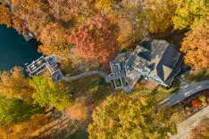 Aerial view of a lakeside house surrounded by trees with autumn foliage colors.