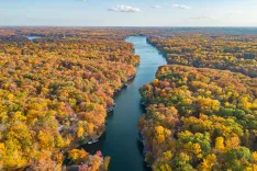 Aerial view of a river winding through a colorful autumn forest with boats docked along the shore.
