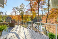 Spacious wooden deck with outdoor furniture overlooking a scenic view of a lake surrounded by autumn foliage.