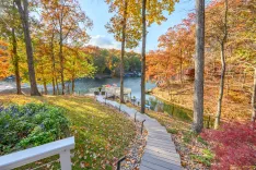 Scenic view of a lakeside with colorful autumn foliage, featuring a wooden pathway leading to a small dock, amidst a peaceful natural setting.