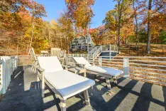 Bright sunny autumn day on a deck with two lounge chairs overlooking trees with fall foliage and a house in the background.