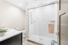 Modern bathroom interior with glass-enclosed shower, white subway tiles, marble countertop, and beige walls.