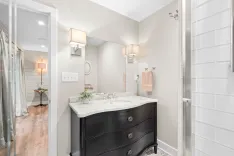 Modern bathroom interior with black vanity cabinet, marble countertop, wall-mounted sink, mirror, and glass-doored shower.
