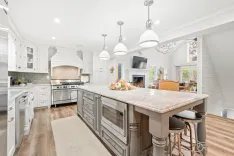 Bright, spacious kitchen with white cabinetry, marble countertops, stainless steel appliances, pendant lights, and a central island with bar stools.