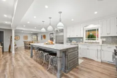 Spacious modern kitchen interior with white cabinets, gray island, stainless steel appliances, pendant lighting, and hardwood floors.