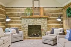 Cozy living room with a rustic stone fireplace, wooden walls, comfortable beige sofas, and decorative lighting.