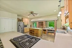 Spacious kitchen interior with modern appliances, wooden cabinets, a central island, brick accents, and pendant lighting.