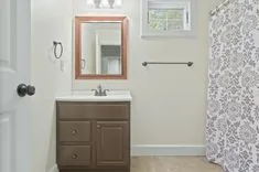 A modern bathroom with a white countertop, brown cabinets, a framed mirror, a patterned shower curtain, and a small window bringing in natural light.