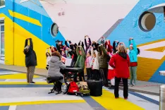 A diverse group of people gathered around a musician playing piano outdoors in a vibrant, colorfully painted urban space.