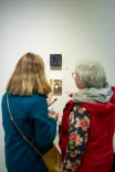 Two women observing and discussing artwork in a gallery setting.