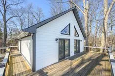  A white modern A-frame house with large windows, surrounded by bare trees, featuring an extensive wooden deck.