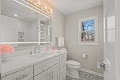 Modern bathroom interior with a large mirror, double sink vanity, and view of trees through the window.