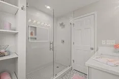 Modern bathroom interior with glass shower, white vanity, and decorative shelving.