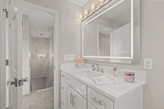 Interior of a modern bathroom with white cabinets, a large mirror, and bright lighting.