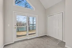 Empty room with gray floors and white walls featuring a closed glass door leading to a deck and a closed solid door on the right.