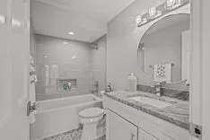 Modern bathroom interior with double sink vanity, large mirror, bathtub, and toilet in grayscale colors.