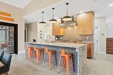 Modern kitchen interior with a stone island, bar stools, pendant lights, and wooden cabinets.