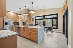 Modern kitchen interior with stainless steel appliances, granite countertops, wooden cabinetry, pendant lights, and tiled flooring.