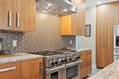 Modern kitchen interior with stainless steel appliances, wooden cabinets, and mosaic tile backsplash.
