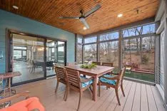 Cozy screened porch with wooden dining set for six, ceiling fan overhead, and a view of bare trees through the screen.
