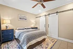 Cozy bedroom interior with a queen-size bed, patterned bedding, a ceiling fan, sliding closet doors, and a nightstand with a lamp.