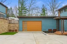 Exterior view of a modern home with a blue facade and wooden garage door, concrete driveway, and a landscaped yard.