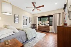 Contemporary bedroom interior with a queen-sized bed, hardwood floors, ceiling fan, and framed pictures on the wall.