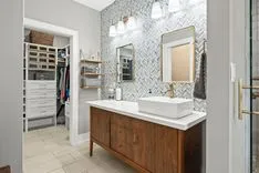 Modern bathroom with patterned wallpaper, wooden vanity with vessel sink, and a walk-in closet in the background.