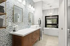 Modern bathroom interior with herringbone patterned tiles, double vanity sink, large mirrors, and a freestanding bathtub.