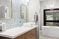 Modern bathroom interior with herringbone tile backsplash, white countertop with vessel sink, wooden vanity, and freestanding bathtub near a window.