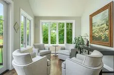 Bright modern living room with white furniture and large windows overlooking greenery.