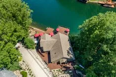 Aerial view of a lakeside house with a red roof surrounded by green trees.