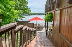 Wooden deck path leading to a patio with a red umbrella overlooking a lake.