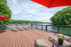 Spacious wooden deck with outdoor furniture under a red umbrella overlooking a tranquil lake.