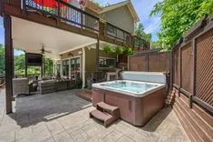 Spacious outdoor patio area with hot tub, seating, and a covered deck of a luxurious house.