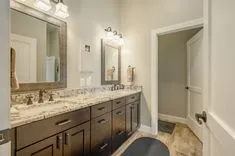 Elegant bathroom interior with double vanity cabinet, granite countertop, large mirrors, and designer lighting.