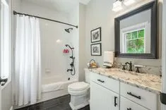 Modern bathroom interior with a white shower curtain, a vanity with a granite countertop, and framed art on the wall.