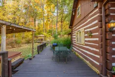 Wooden cabin exterior with deck and patio furniture surrounded by autumn trees.