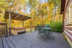 Wooden deck of a house with outdoor furniture and a hot tub surrounded by trees with autumn foliage.