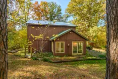 Secluded brown cabin surrounded by autumn trees with sunlit foliage.