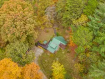 Aerial view of a secluded cabin surrounded by dense autumn-colored woodland.