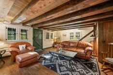 Cozy rustic-style living room interior with leather sofas, a patterned rug, wooden beams, and a staircase.