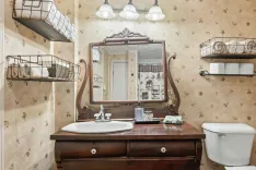 Elegant bathroom interior with patterned wallpaper, a wooden vanity cabinet, decorative mirror, and pendant lights.