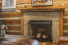 Cozy cabin interior with a stone fireplace, log walls, and wooden mantel displaying decorative items.