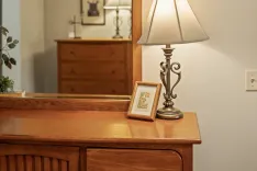 Cozy interior corner with a vintage lamp and a framed picture on a wooden dresser.