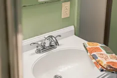 A bathroom sink with a silver faucet and a colorful hand towel on the countertop, pale green walls and an electrical outlet in the background.