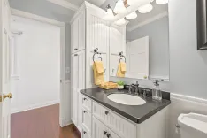 Elegant bathroom interior with white cabinetry, black countertop, oval mirror, and terracotta tile flooring.