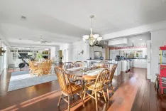Spacious dining area with a wooden table set for a meal, hardwood floors, and an open plan kitchen with white cabinetry and modern appliances, bright natural lighting, and a white ceiling fan.