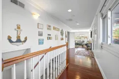 Bright, nautical-themed hallway with wooden floors, white walls adorned with lake-inspired decor, and a view into a cozy living room.