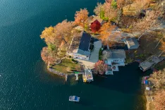 Aerial view of a lakeside property with a house surrounded by autumn-colored trees, a boat dock, and a boat on the water.